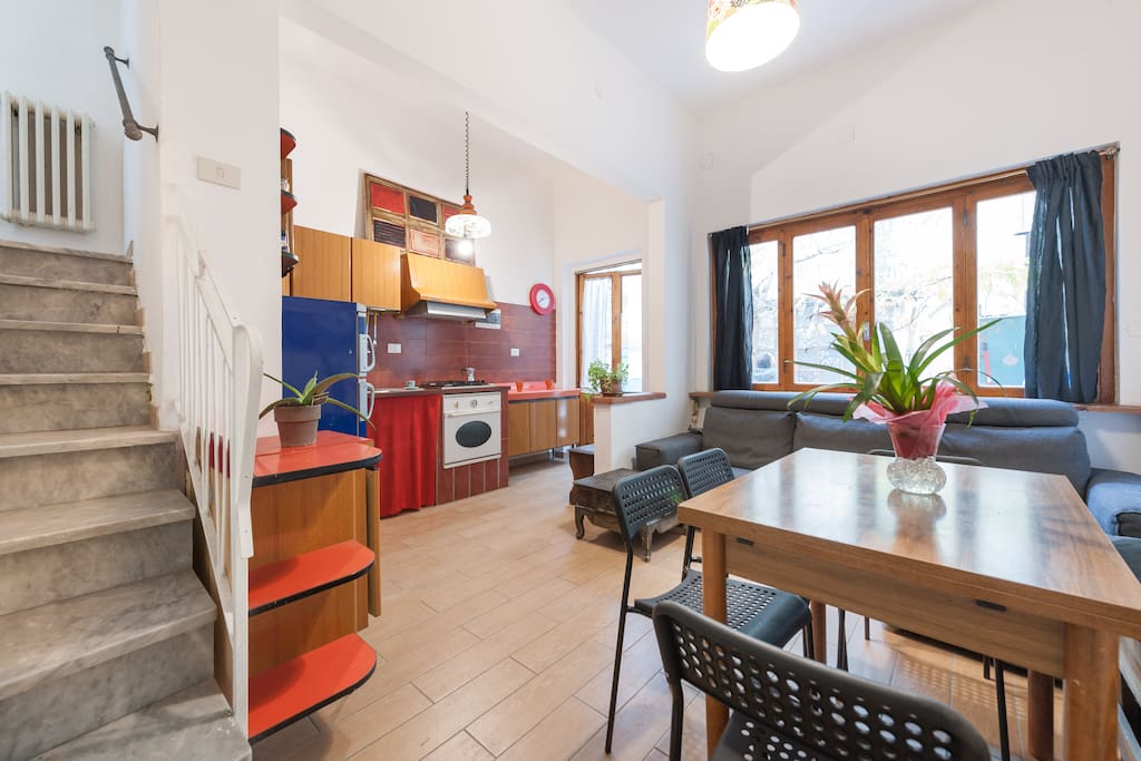 Pian terreno con cucina accessoriata zona soggiorno con divano e sala da pranzo con finestre su giardinetto interno.