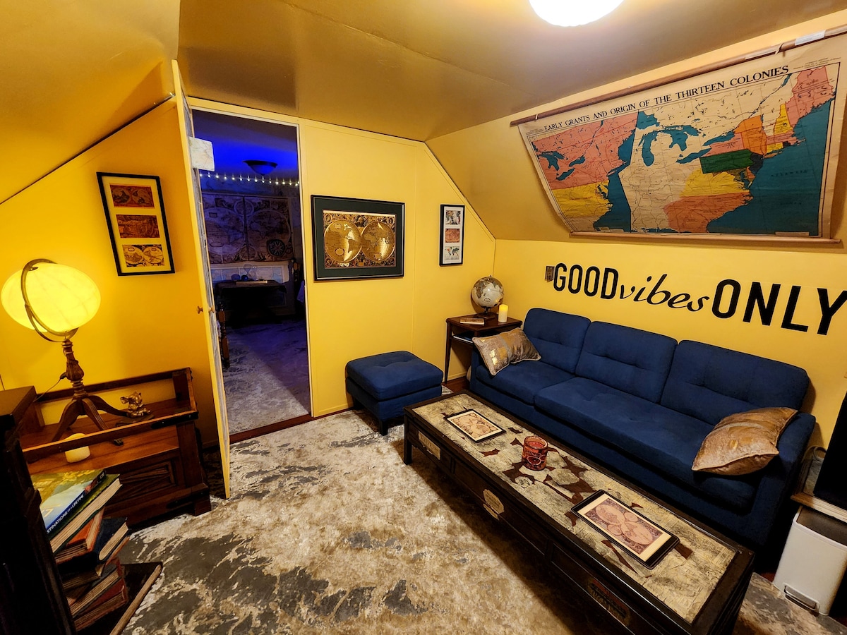 A cozy sitting area features a blue couch and a vintage wooden coffee table, surrounded by bright yellow walls. A globe highlights the space, while a map decorates the wall. Soft light creates a warm atmosphere, enhancing the inviting feel of the room.
