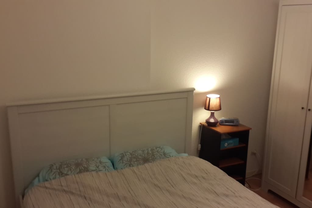 La chambre privée avec son grand lit 2 places, une table de nuit et une armoire