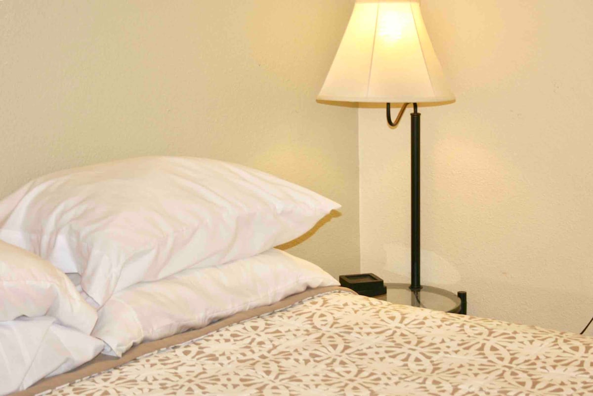 Cama tamaño queen y soporte de lámparas en el dormitorio. 