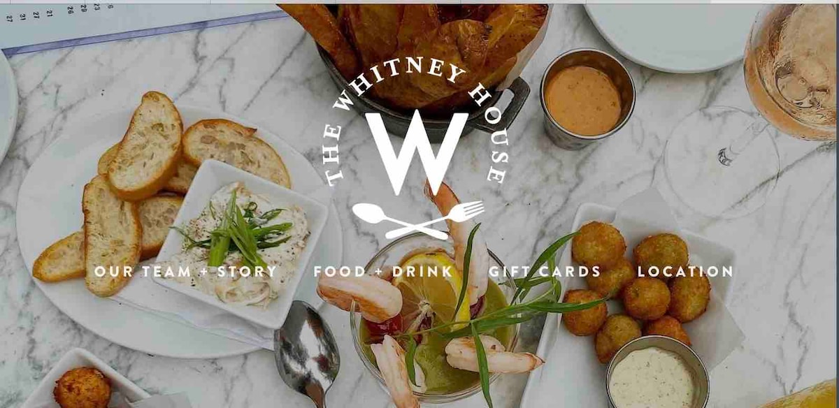 An assortment of dishes is displayed on a white marble table. Crispy golden potatoes accompany a bowl of creamy dip and a vibrant cocktail. Shrimp and green garnish are arranged elegantly, while a bowl of golden-brown appetizers is included, showcasing a variety of textures and colors.