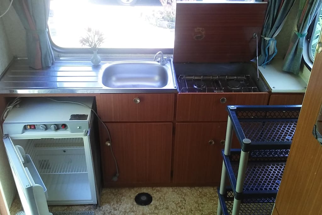 Kitchenette with tap, sink, stove, fridge, storage and utensils.