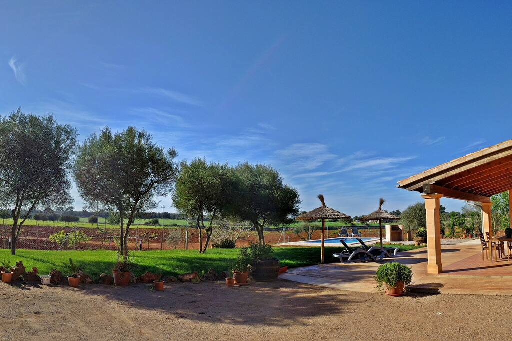 Imagen de la entrada a la propiedad en la que los huéspedes podrán estacionar su vehículo. Además, en esta imagen podemos apreciar la zona de jardín, la terraza de la casa y la zona de la piscina.