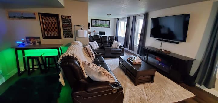 Living room with recliner couches that have USB charging ports and cup holders.  Virtual Reality gaming space with Oculus Quest 2 headset.  Electric fireplace with multiple flame color choices, and a portable air conditioning unit.