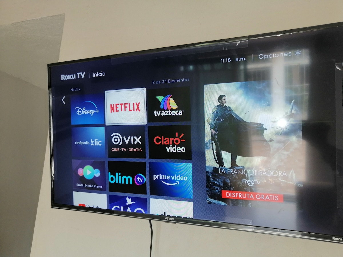 A wall-mounted television displays various streaming service icons, including Netflix and Disney+. The user interface shows a main menu with highlighted selections and an image from a movie. The screen appears to be modern and centrally positioned for viewing.