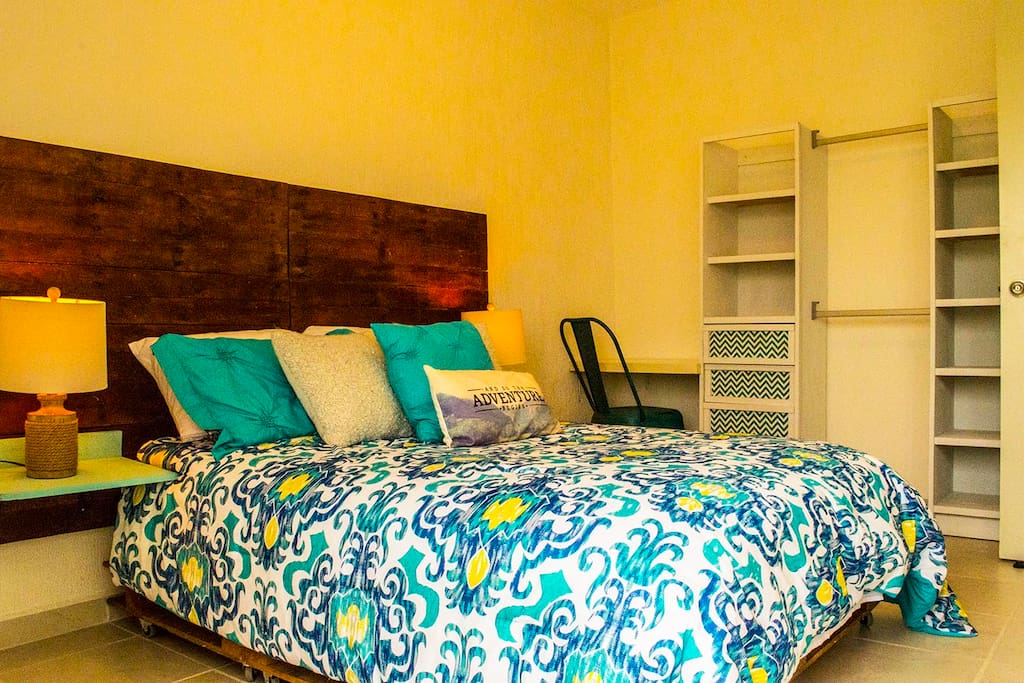 Recámara principal con cama Queen, cuenta con aire acondicionado, perchas para ropa y un pequeño escritorio.