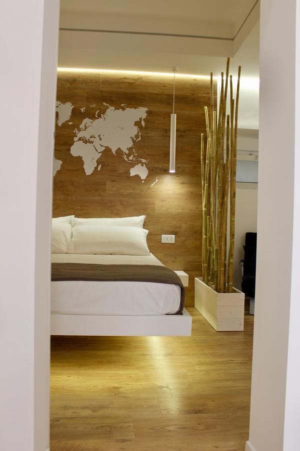 A bright sleeping area showcases a spacious bed with crisp white linens against a wood-paneled wall featuring a world map. Bamboo plants in a wooden planter add a touch of greenery, while subtle lighting enhances the room's serene ambiance.