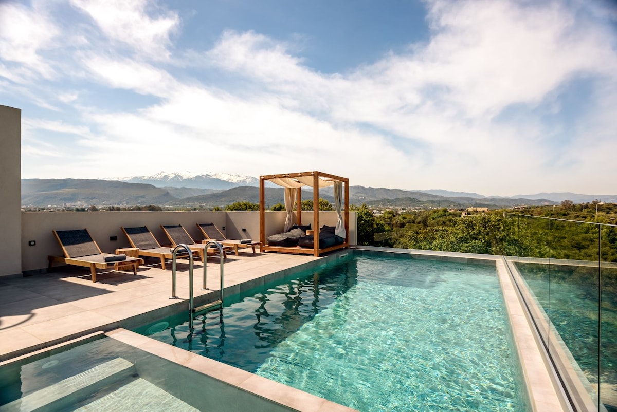 An inviting rooftop pool is surrounded by panoramic views of the mountains. Comfortable lounge chairs are positioned nearby, and a shaded cabana offers a cozy spot for relaxation. The clear water reflects the blue sky, creating a refreshing atmosphere for guests.