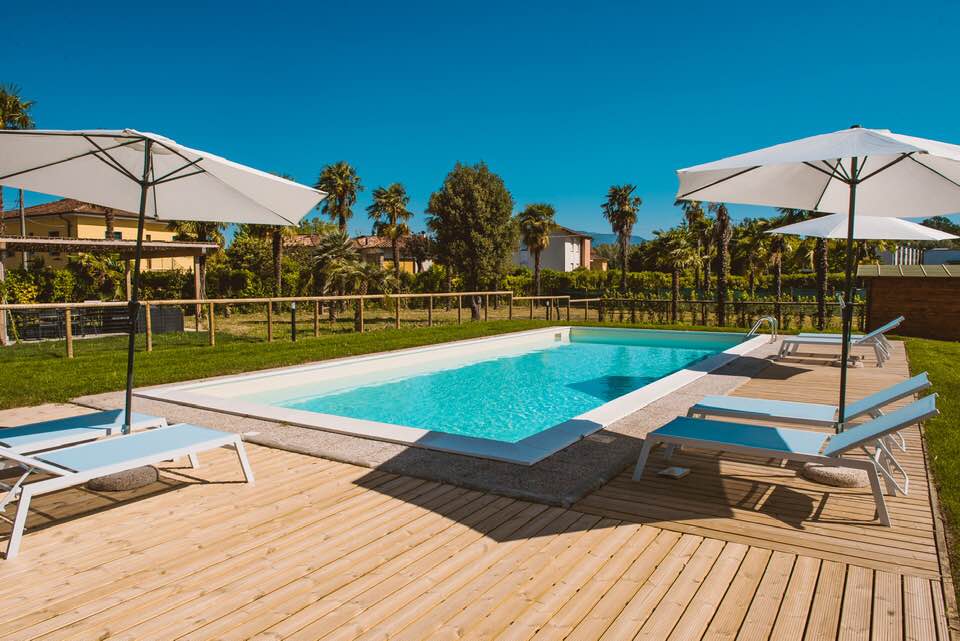 A serene salt-water pool is framed by wooden decking, with comfortable lounge chairs and umbrellas positioned for shade. Lush greenery and palm trees surround the area, contributing to a private and relaxing outdoor space.