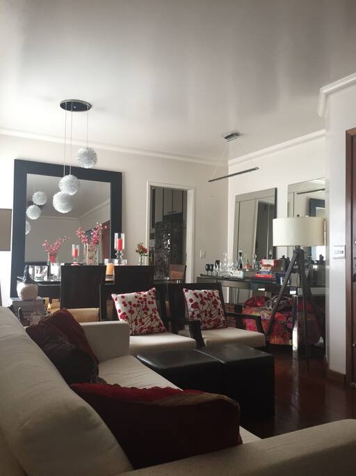 Sala aconchegante com TV, sofá, duas poltronas e mesa com seis cadeiras. O ambiente tem claridade e fomenta acolhimento. Os espelhos são de manutenção do proprietário e pedimos não tocá-los por motivo de preservação.