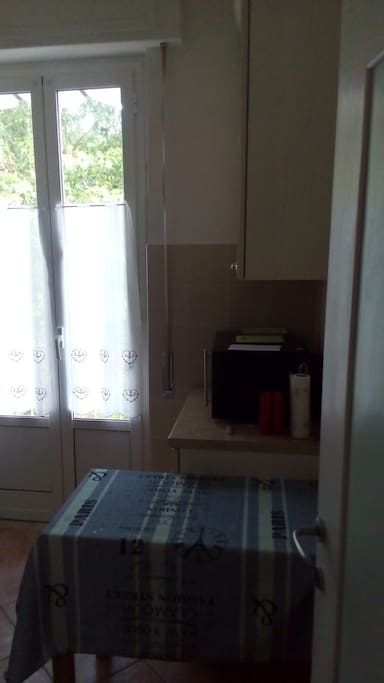 Ingresso della cucina, con piccolo tavolo, forno a micronde e finistra che dà su un piccolo balcone.