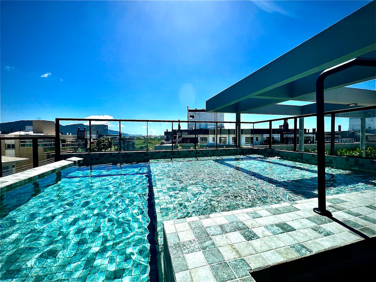 An inviting rooftop pool is surrounded by tile decking, capturing sunlight throughout the day. A glass railing provides safety while offering unobstructed views of the surrounding area. The pool's clear water sparkles, suggesting a refreshing atmosphere for relaxation.
