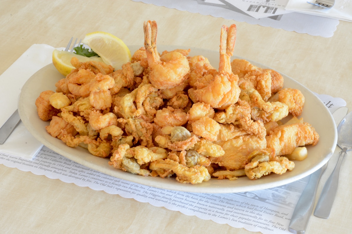 A large oval platter is filled with a variety of fried seafood, including shrimp and fried fish. Fresh lemon wedges are placed alongside, adding a touch of brightness to the presentation.