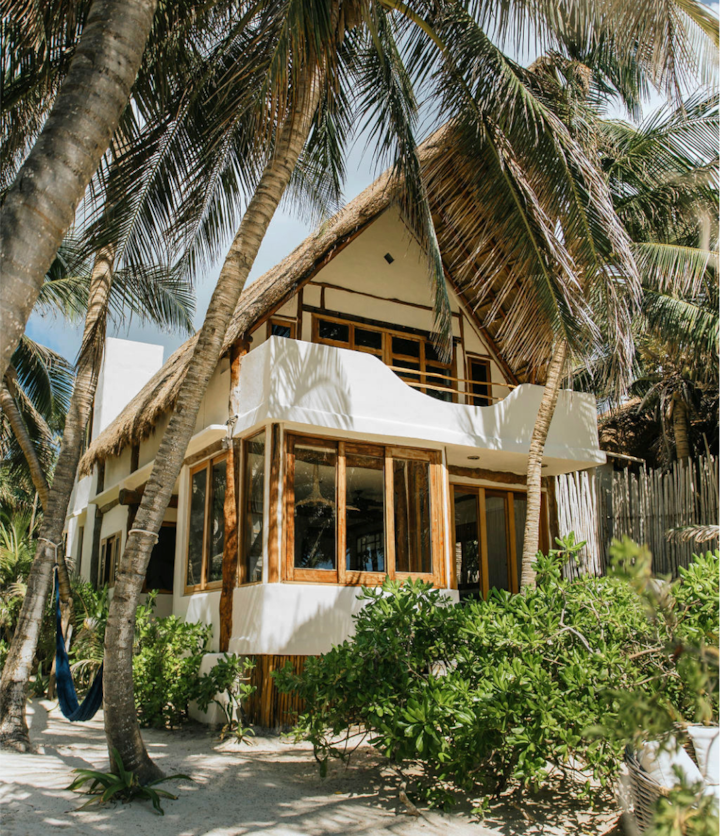 A sunlit patio of a beachfront villa in Sian Kaan reserve complete with shaded lounge seats, palm-thatched canopy, and a few subtle steps leading into a glistening pool.