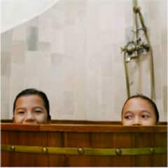 Two young kids peeking over the edge of a wooden bathtub.