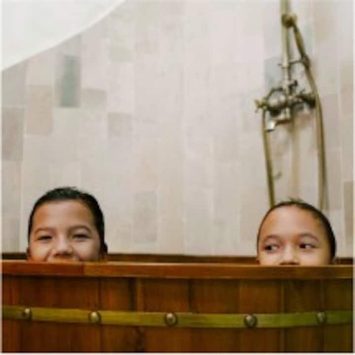 Two young kids peeking over the edge of a wooden bathtub. 