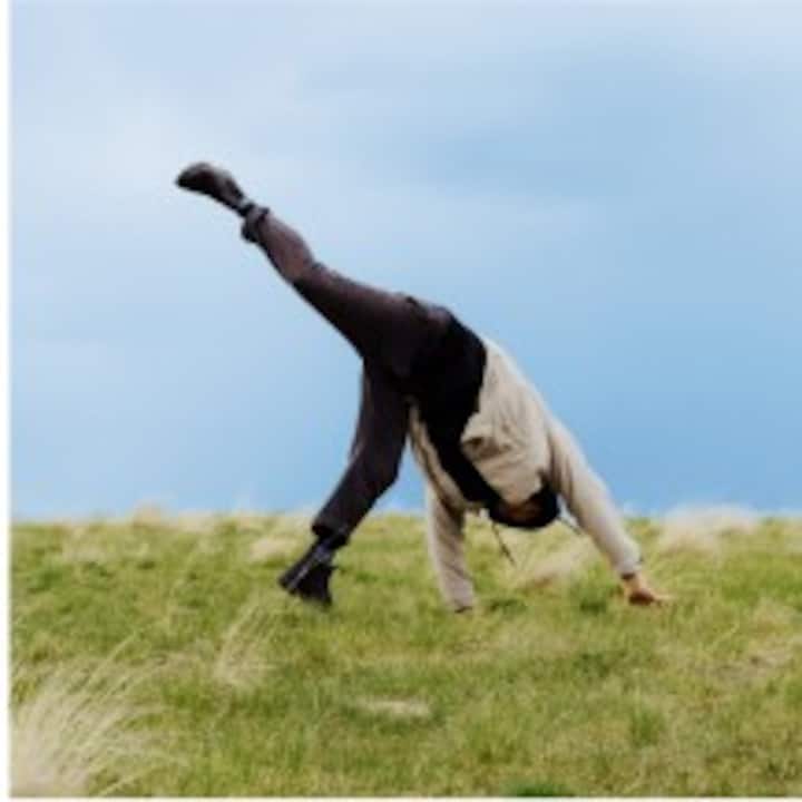 A person doing a cartwheel in a green field under a blue sky.