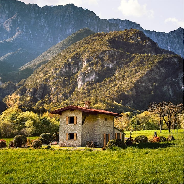 A stone farmhouse in Italy in front of tall hills and cliffs. 