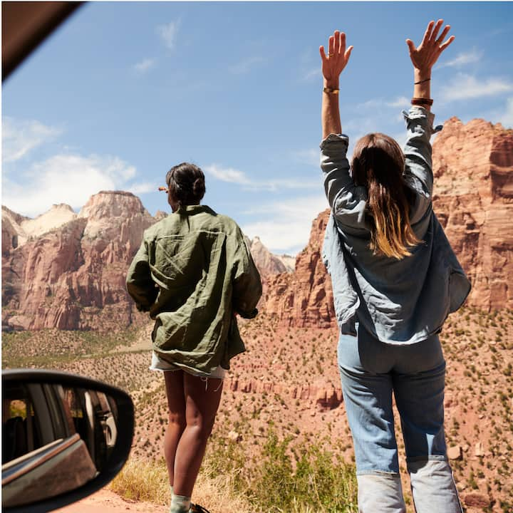 View from inside a car looking out at two women facing a rocky desert landscape.