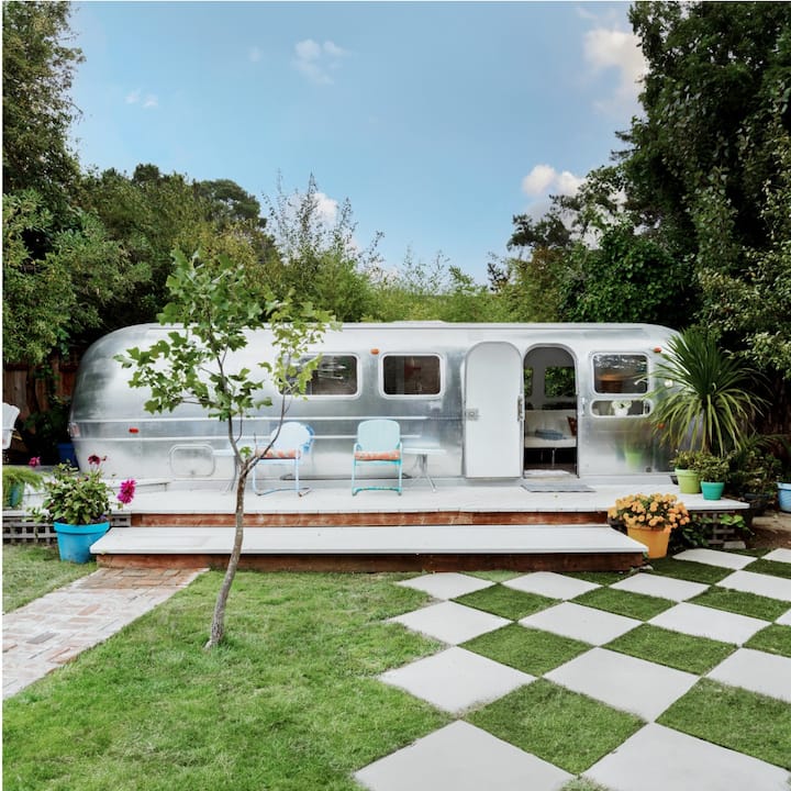An airstream trailer with a front deck and two chairs overlooking a checkerboard lawn. 