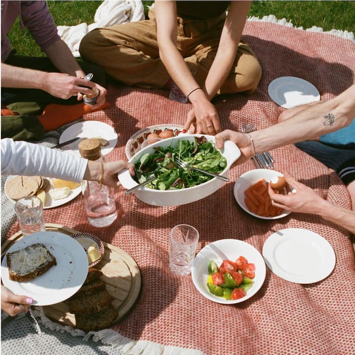 Four people on a picnic blanket sharing a meal.