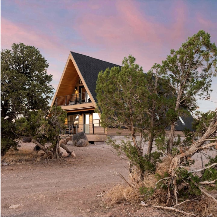 An A-frame house at sunset in a desert landscape. 