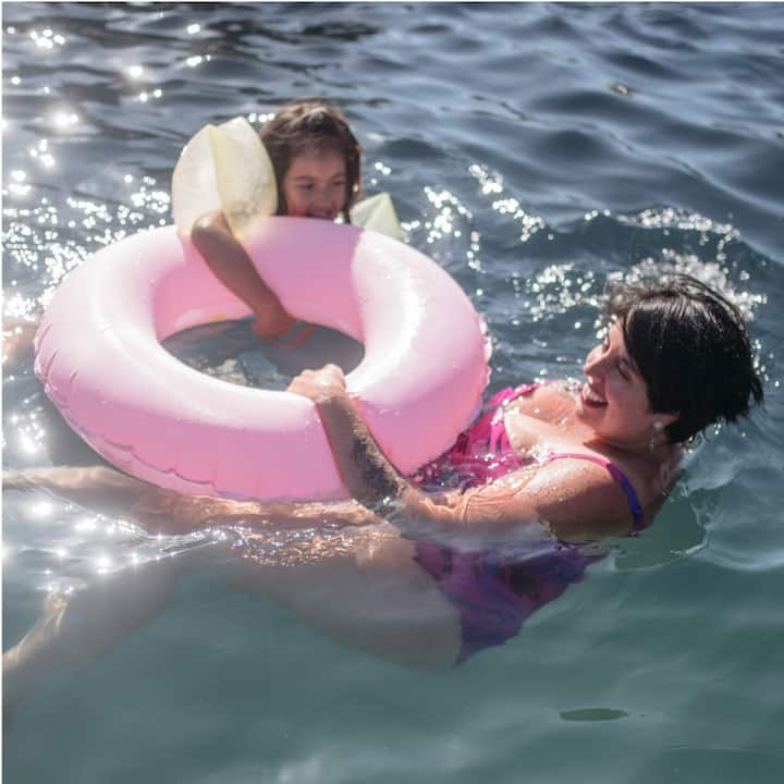 A woman and girl swimming and holding onto a pink innertube.