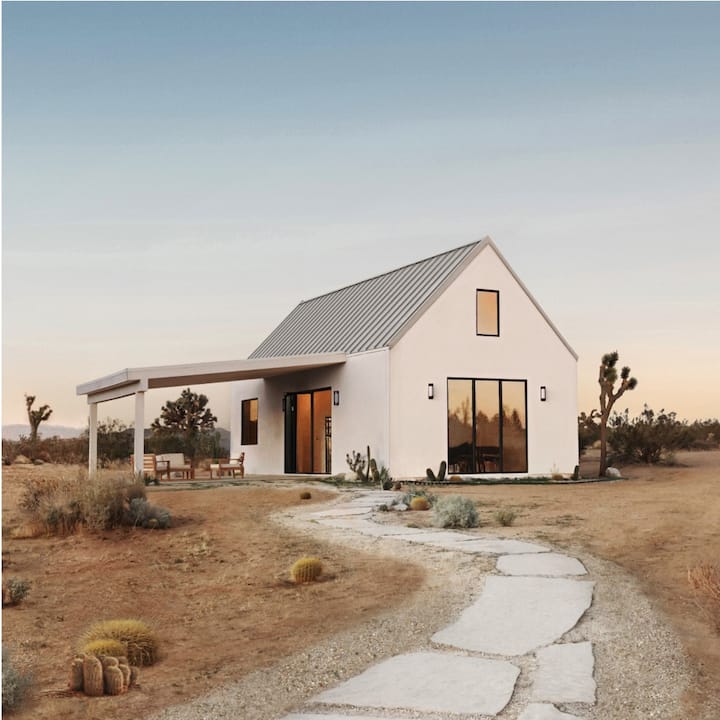 A white two-story home with a porch in a desert landscape. 