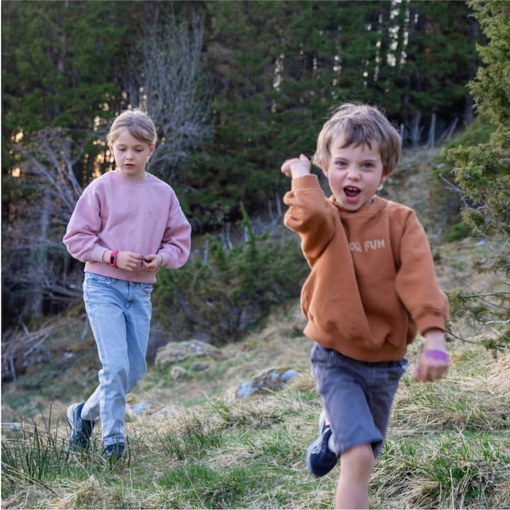 A boy and girl walking on a hillside in the woods.