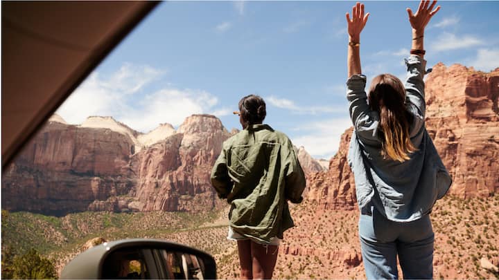 View from inside a car looking out at two women facing a rocky desert landscape.