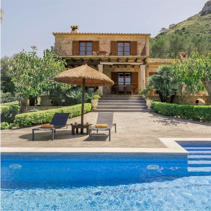 A two-story stone house with a swimming pool and palm trees. 