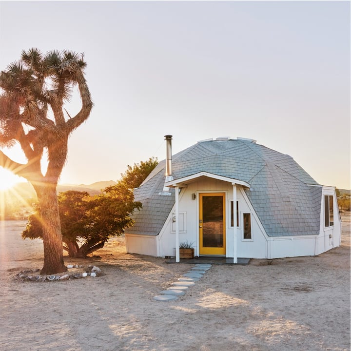 Sunrise over a white-domed cabin in the desert.