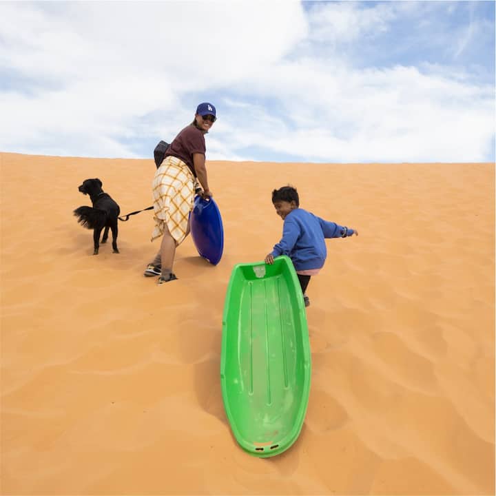 A family and their dog get ready to go sledding on a sand dune.