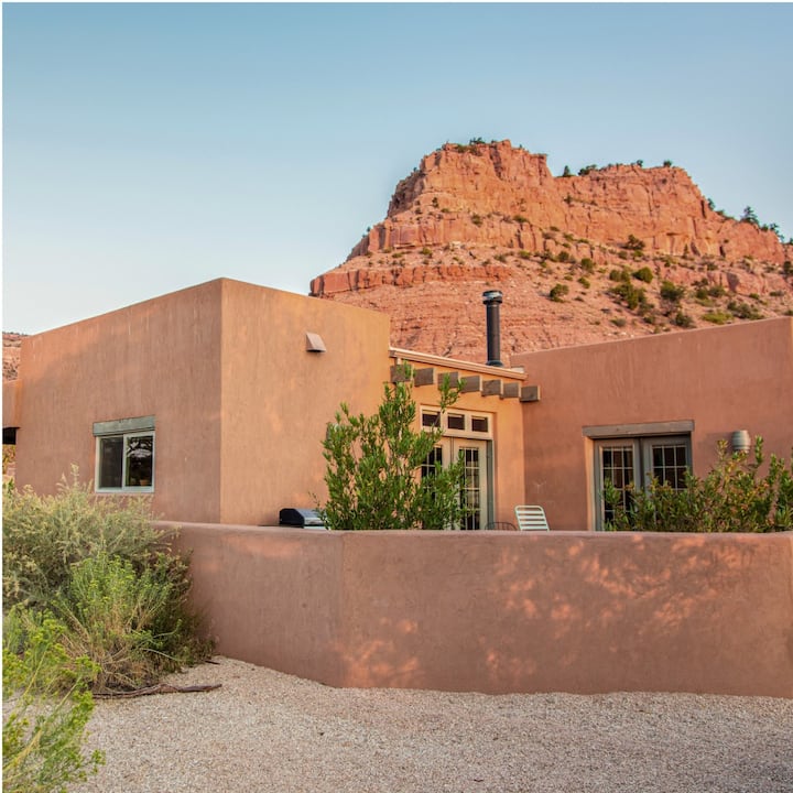 An orange adobe house in front of a rocky hill.