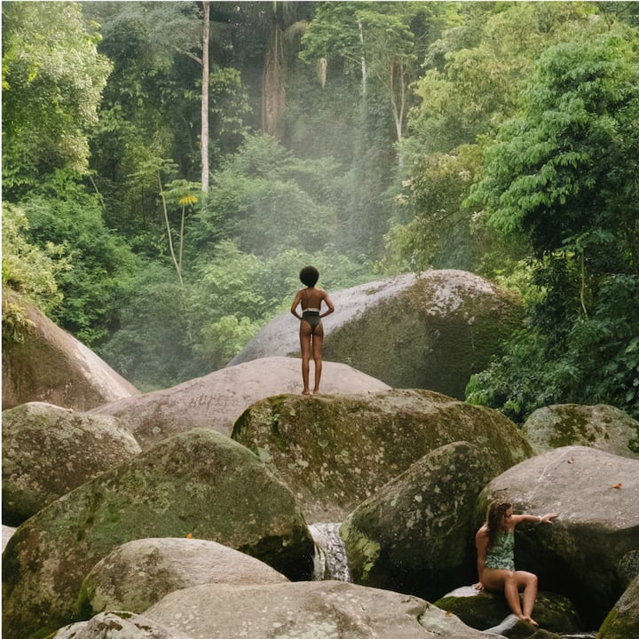 Two children play in the river on big mossy rocks.