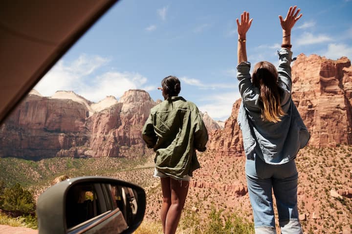 View from inside a car looking out at two women facing a rocky desert landscape.