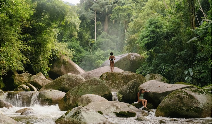 Two children play in the river on big mossy rocks.