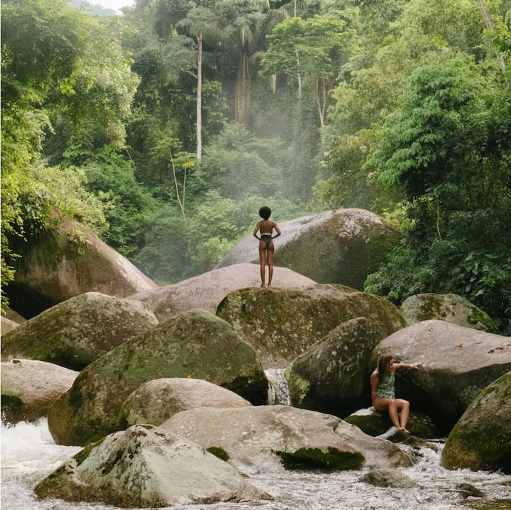 Two children play in the river on big mossy rocks.