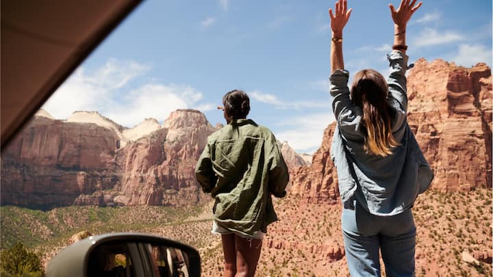 View from inside a car looking out at two women facing a rocky desert landscape.