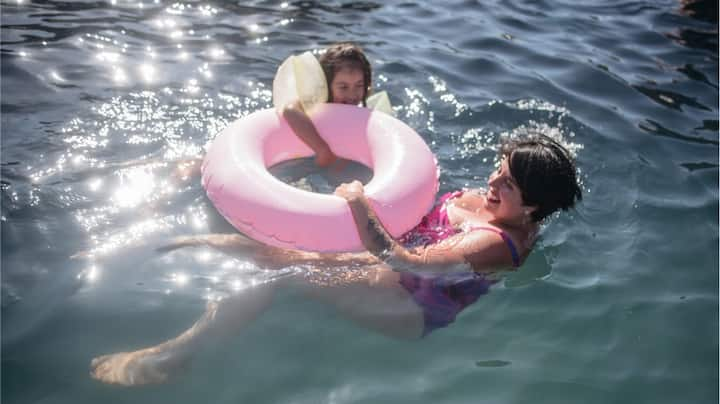 A woman and girl swimming and holding onto a pink innertube.