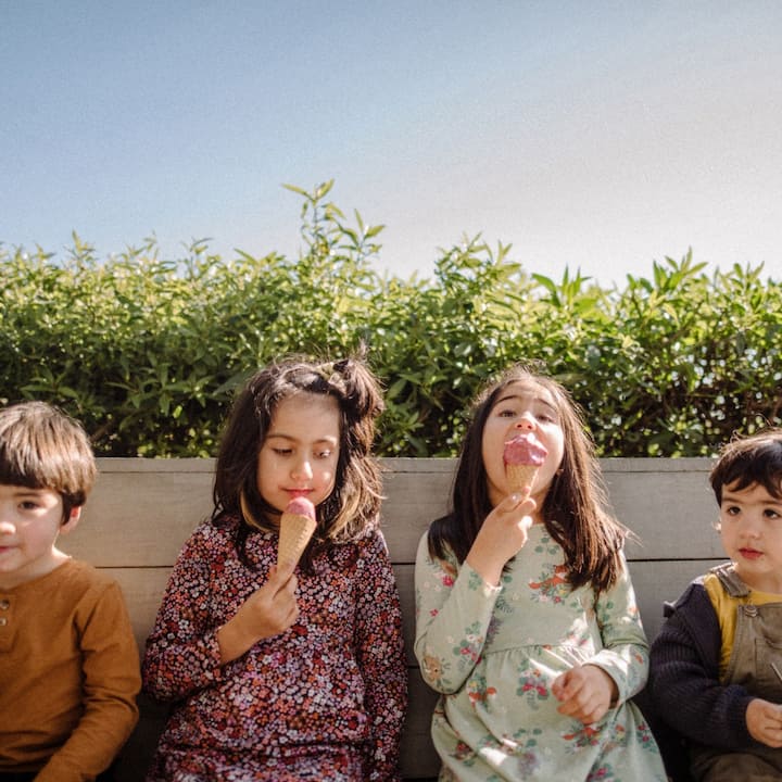 Four children sitting on a bench eating ice cream. 