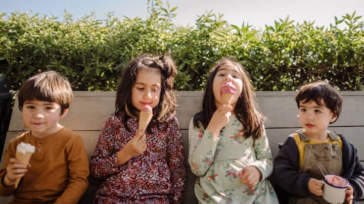 Four children sitting on a bench eating ice cream. 