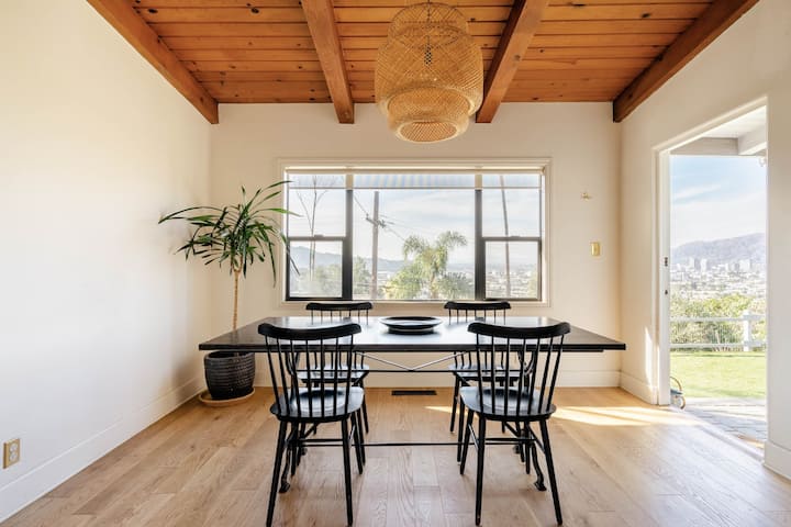 Una mesa de comedor con una lámpara de mimbre que cuelga justo encima. Es un bonito y cálido día de verano. El techo de la habitación es de madera.