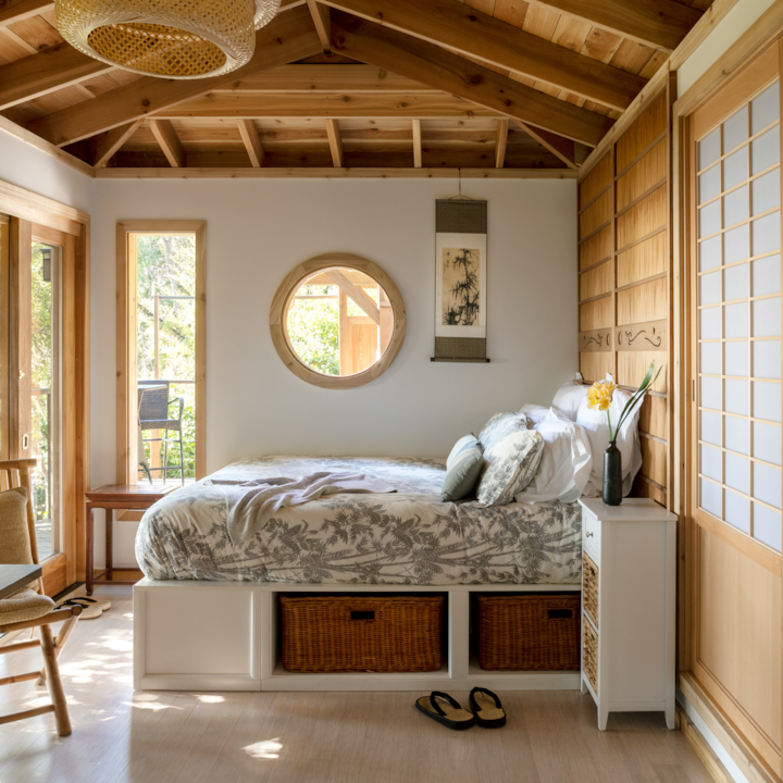 Une chambre au style japonais. Recouvert d'une couette, le lit est bordé soigneusement. La pièce dispose d'une fenêtre circulaire donnant sur une cour verdoyante.