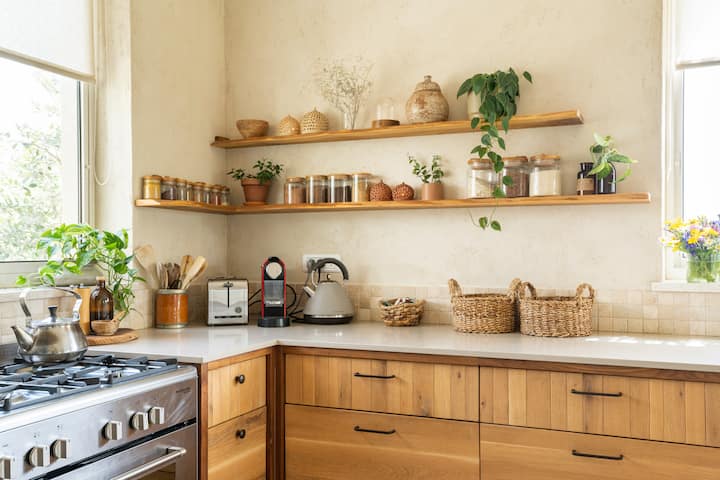 Warme keuken met mooie houten laden. Op een romig, marmeren aanrechtblad staat wat keukenapparatuur. Alles is opgeruimd en overzichtelijk.