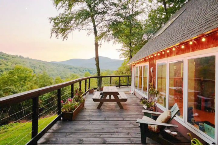 A view from the deck of a red-barn looking house in a rural area. It has string lights turned on and is setting the mood in the evening light.