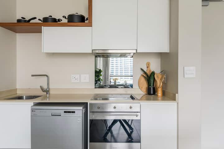 A small beige kitchen. It looks like it could be a kitchen in a studio apartment. There are 3 pots in a row up on a shelf. There are very few items on the counter tops, making for a nice tidy surface.