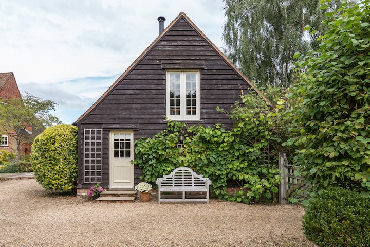 The exterior of the front entrance of the house. It is brown and A-framed. It looks like a quaint farmhouse. There are well-kept bushes surrounding the house.