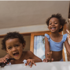 Two young children play happily on the edge of a bed.
