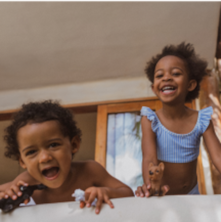 Two young children play happily on the edge of a bed. 